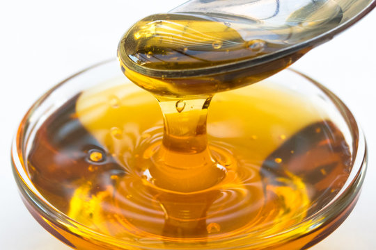 Healthy organic bee honey falling into glass jar. Spoonful of honey Isolated 