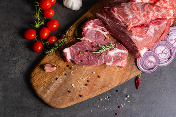 raw meat and vegetables on cutting board on dark cement background