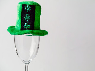 Green hat with shamrock on empty wine glass and bright background., Saint Patrick day celebration concept. Vertical image.