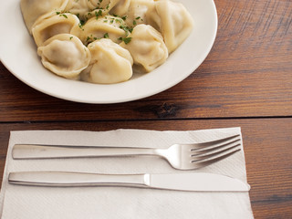 Portion of traditional large dumplings with meat on a white plate and fork and knife on a white napkin.