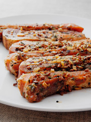 Serving of raw uncooked pork belly slices in soy marinade and herbs on a white plate