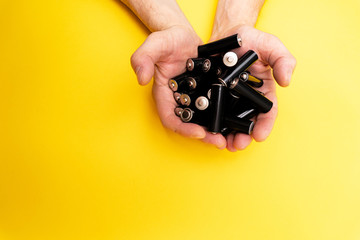 A lot of black aa batteries in male hands on yellow background, view from the top, minimal concept,...