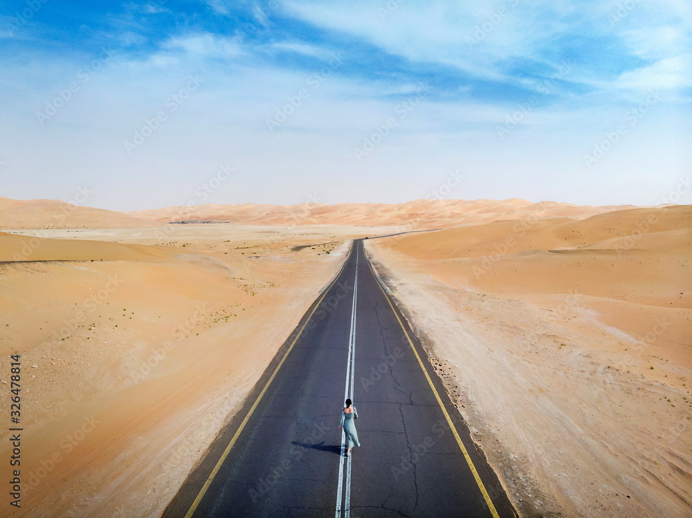 Wall mural woman walking on the scenic dessert road