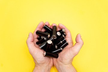 Pile of black aa batteries in mans handful on yellow background, view from the top, minimal...