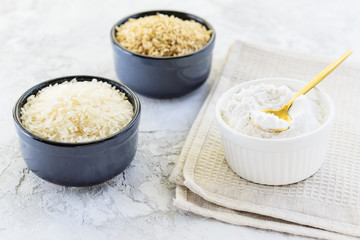 Rice flour in a bowl on a napkin with white and brown rice. Gluten free, healthy diet concept.