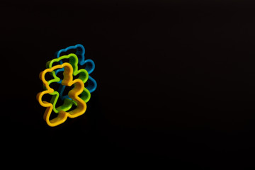 Three multi-colored plastic cookie cutter for making cookies in the form of a teddy bear on a black...