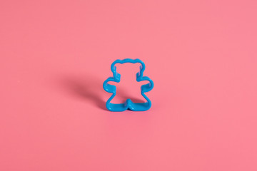 Blue plastic cookie cutter for making cookies in the shape of a teddy bear on a pink background....