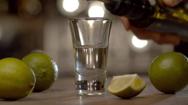 Making a short drink red dog. Close up bartender pouring tequila and sambuca into a glass, then adding Tabasco. Bar counter on the background of blurry light bulbs.