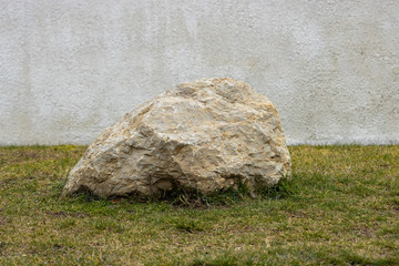 The large stone  on the grass .White wall in the background.
