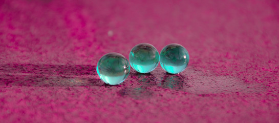 Three shiny glass beads in turquoise. Like three worlds. Pink rough faint background. Copy space.