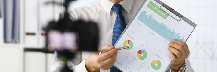 Portrait of smiling blogger in classic suit and tie showing statistics data with graphs charts...