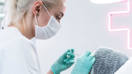 The young beautician doctor preparing to making injection in female forehead. The doctor...