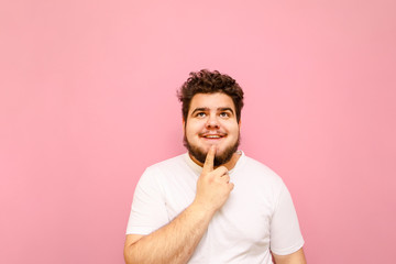 Portrait of a funny happy fat man in white t-shirt on a pink background, looks up at copy space...
