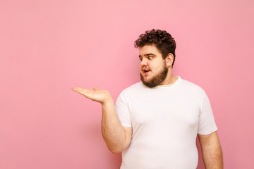 Surprised guy with overweight, curly hair and a beard holds copy space in his hands and looks at...