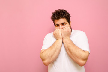 Frightened guy in a white T-shirt and curly overweight hair, looks into the camera and covers his...