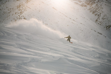 Snowboarder in full equipment rides on a snowboard in mountains
