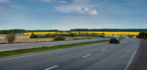 Road and yellow blooming rape fields on background. Picturesque spring scenery.