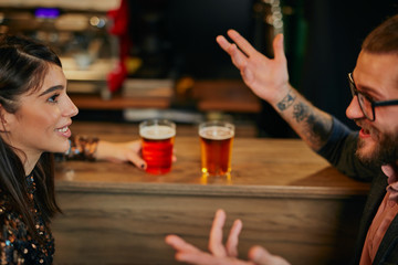 Caucasian couple leaning on bar counter, drinking beer and chatting. Nightlife. Pub interior.