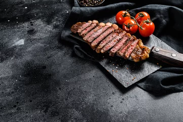 Selbstklebende Fototapeten Grilled sliced strip loin steak on a meat cleaver. Black background. Top view. Copy space © Vladimir