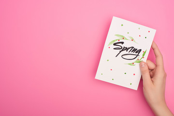 Cropped view of woman holding card with spring lettering on pink background