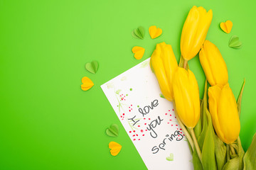Top view of yellow tulips, card with I love you spring lettering and decorative hearts on green background