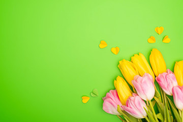 Top view of yellow and pink tulips with decorative hearts on green background, spring concept