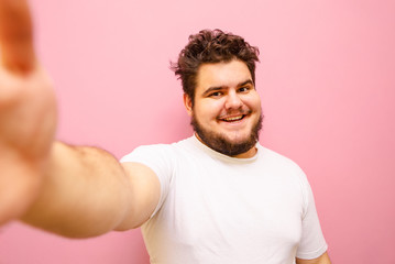 Happy overweight man taking selfie on pink background, looking into camera and smiling. Funny fat...