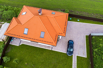 Aerial top view of house shingle roof with attic windows and black car on paved yard with green...