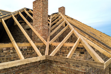 Private residential house with wooden roof frame structure under construction. Unfinished brick building under development.