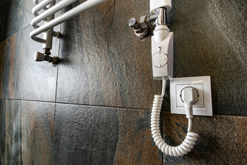 White contemporary electric towel dryer mounted on black tiled wall in modern bathroom.