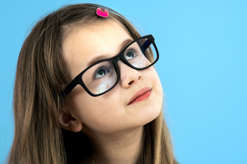 Close up portrait of a child school girl wearing looking glasses isolated on blue background.