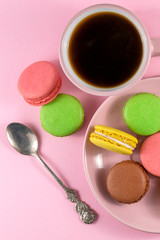 .colored macaroons on a plate and a cup of coffee on a pink background