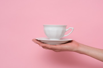 Fototapeta na wymiar Coffe please. Female hand holding a cup of coffee isolated on pink background. Time to charge battery.