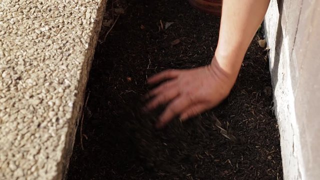 close up  of a mature woman's hand composting the soil and moving the dirt from side to side to merge the soil with the fertilizer