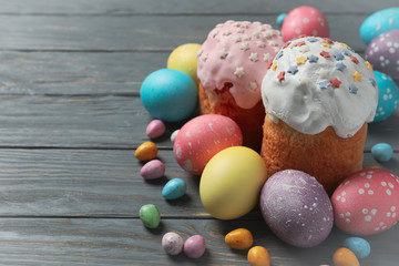 Easter eggs and cakes on grey wooden background, space for text
