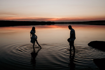 Young couple in the water on Sunset. Two silhouettes against the sun. Romantic love story.