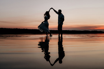 Young couple dancing in the water on Sunset. Two silhouettes against the sun. Romantic love story. - Powered by Adobe