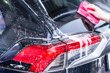 Girl cleaning automobile with sponge at car wash, car washing