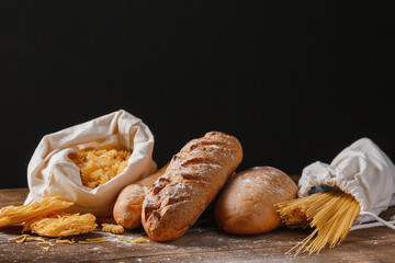 Variety of types of Italian pasta and bread on wooden background.