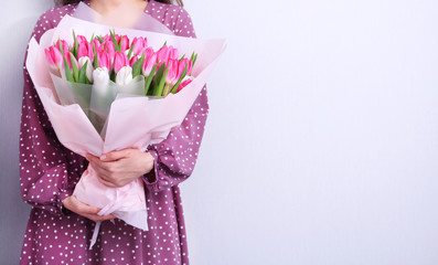 Portrait of a young woman in purple dress holding bouquet of pink and white tulips on grey background.Spring greeting card. Background.Easter,spring flower concept.Mothers or Womans day.
