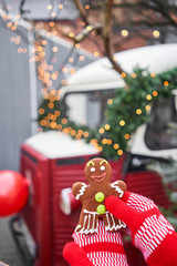 Hand in red mitten holding a smiling gingerbread man and christmas mood in blurred background. Christmas market in old town European small city.