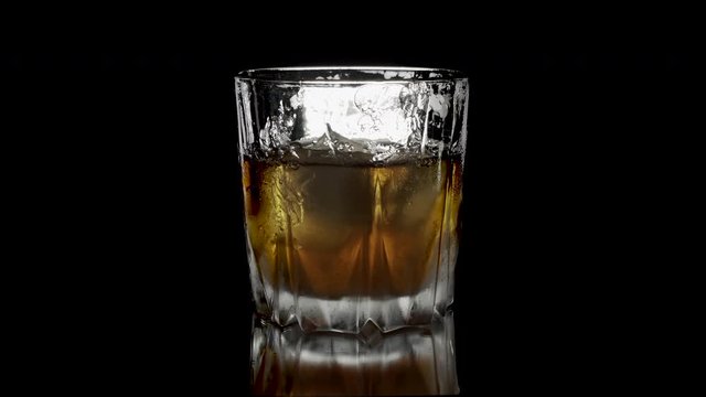  Ice cubes rotating and melts in a glass of whiskey. Isolated on black background. Rotating ice bubes in  whiskey on a white background 