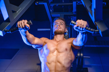 Shirtless young bodybuilder doing bench press for chest. Strong abs. Blue light filter. Photo from...