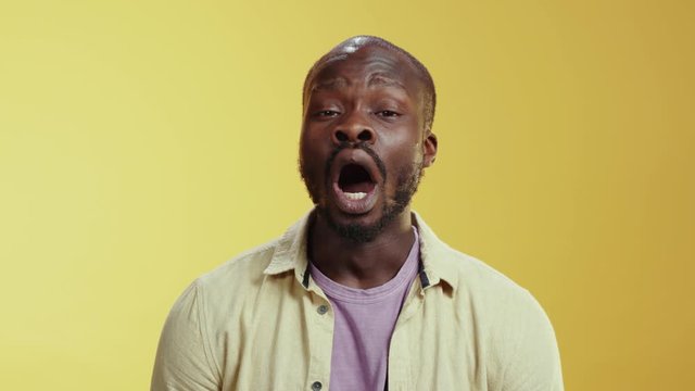 Tired african american man yawning wants to sleep expressing disinterest and apathy posing at yellow wall background. Copy space.