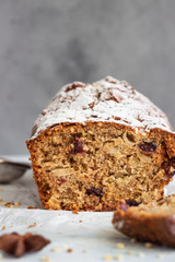 Spicy apple, nuts and dried cranberry loaf cake decorated with powdered sugar on a paper.