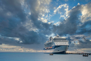 Fototapeta na wymiar A massive luxury blue and white cruise ship at a dock in the tropics under a storm cloud