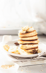 Pancakes with banana, honey and nuts on ceramic plate, sunny shadowed table surface. Natural light and shadows food photography concept. Breakfast.