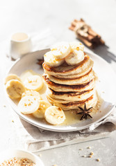 Pancakes with banana, honey and nuts on ceramic plate, sunny shadowed table surface. Natural light and shadows food photography concept. Breakfast.