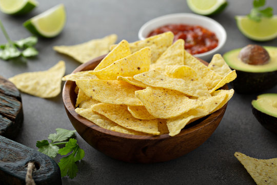 Tortilla chips in a bowl with salsa, limes and avocados
