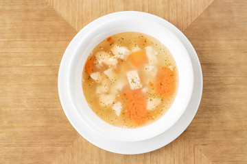 Fish soup in a white plate. Fish soup with vegetables, celery in a cup for the broth. Pike perch and salmon. Plate on wooden table. Restaurant menu